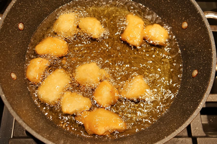 A frying pan with coated chicken pieces being fried in hot oil.