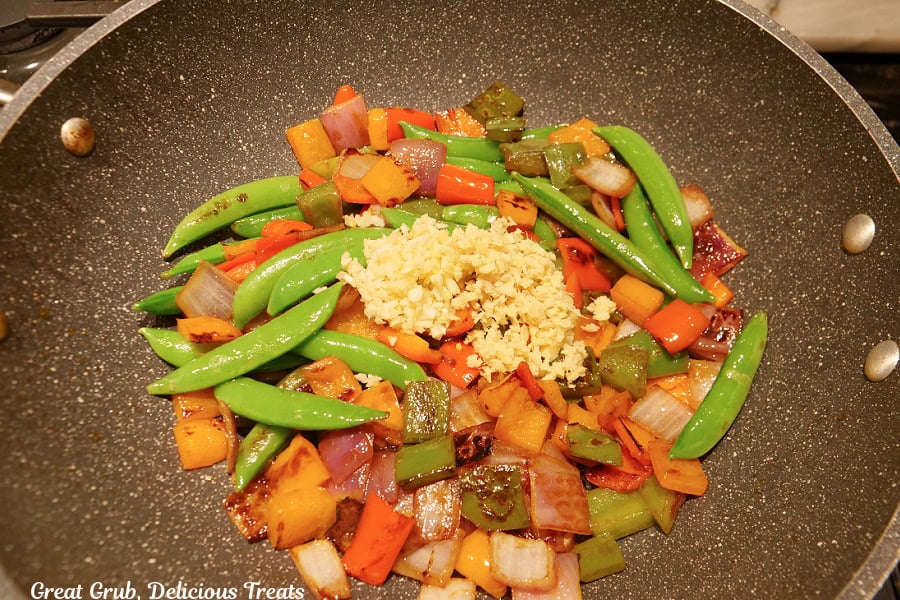 A frying pan with stir-fry vegetables in it with minced garlic on top.