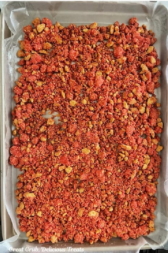 A parchment lined baking sheet with strawberry crunch topping on it after being baked.