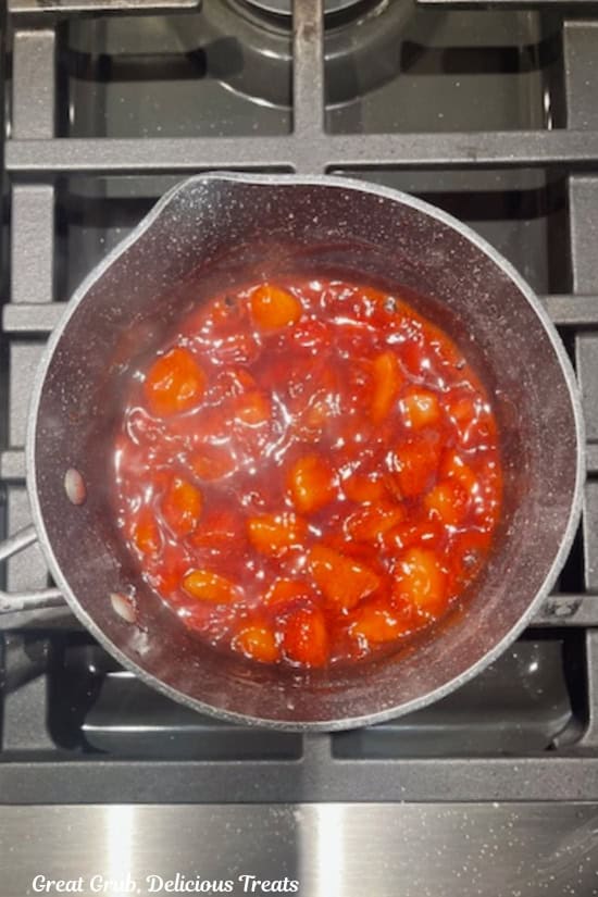 A saucepan on the stove with fresh strawberries filling in it.
