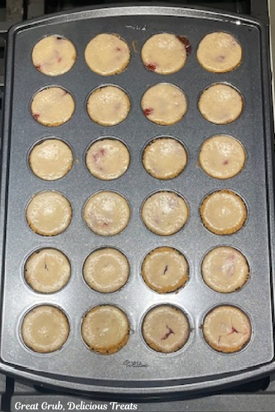A 24-count mini muffin pan with baked mini cheesecakes in it.
