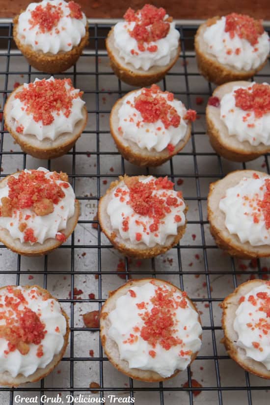 A wire cooking rack with mini strawberry crunch cheesecake bites on it.