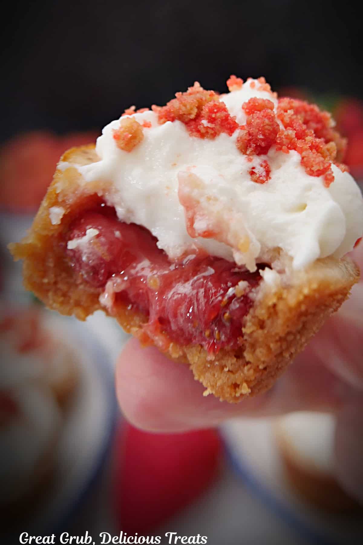A close up photo of a mini strawberry crunch cheesecake bite with a bite taken out of it.