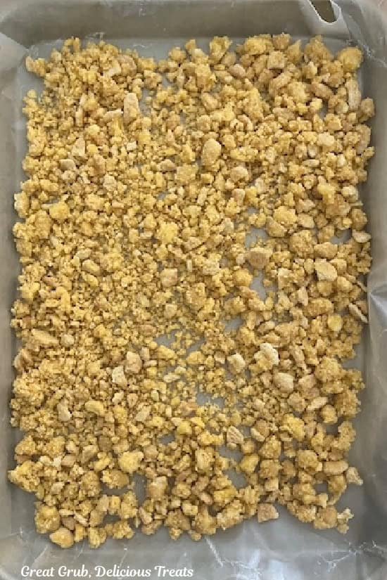 A parchment lined baking sheet with lemon crunch spread out on it in a single layer.