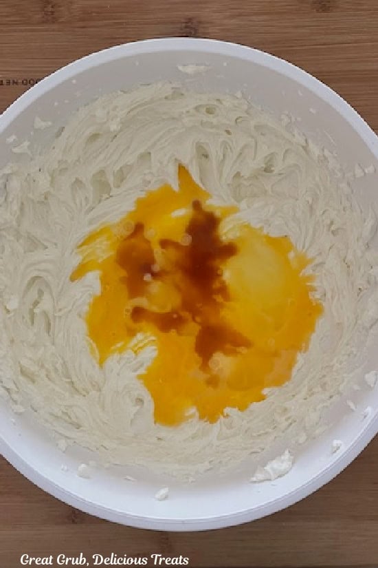 A white bowl with cream cheese that has been beaten then vanilla and an egg added.