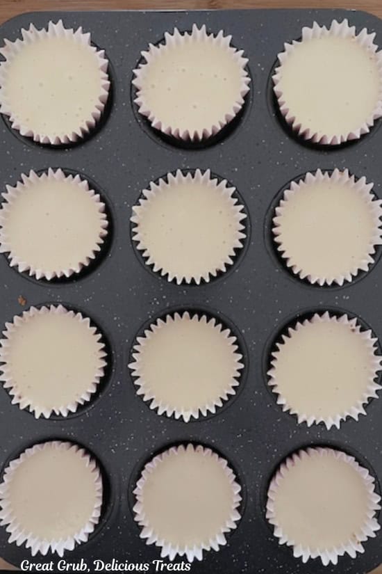 A 12-count muffin tin with the cheesecake batter in the cupcake liners.