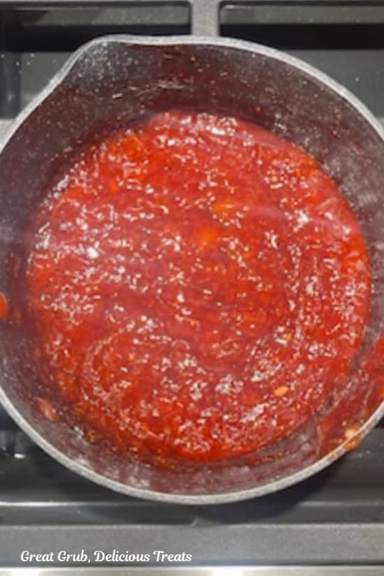 A saucepan with fresh strawberry topping boiling in the pan.