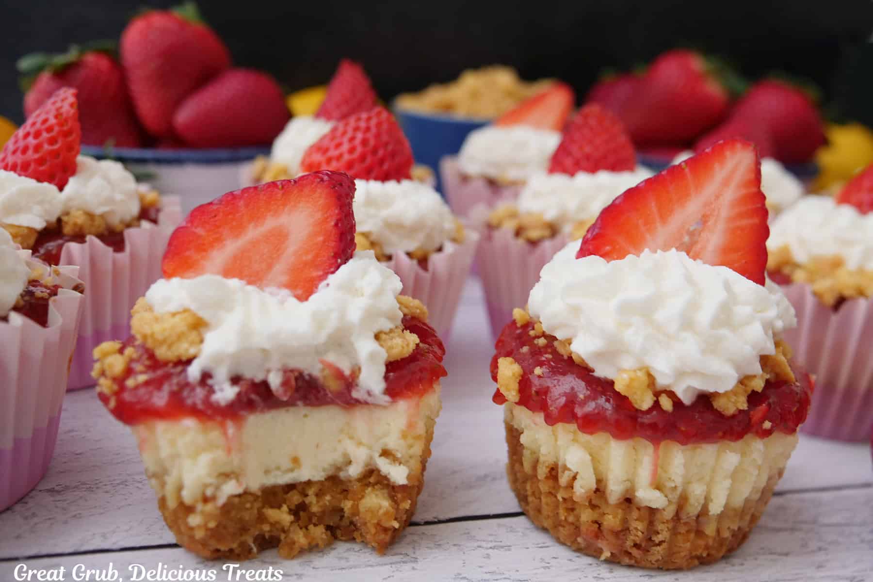 A white surface with mini strawberry lemon crunch cheesecakes on it with a bite taken out of one of them.
