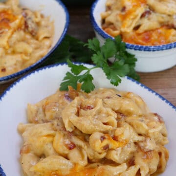 A wood surface with three white bowls with blue trim filled with bacon mac and cheese, and a title overlay at the top.