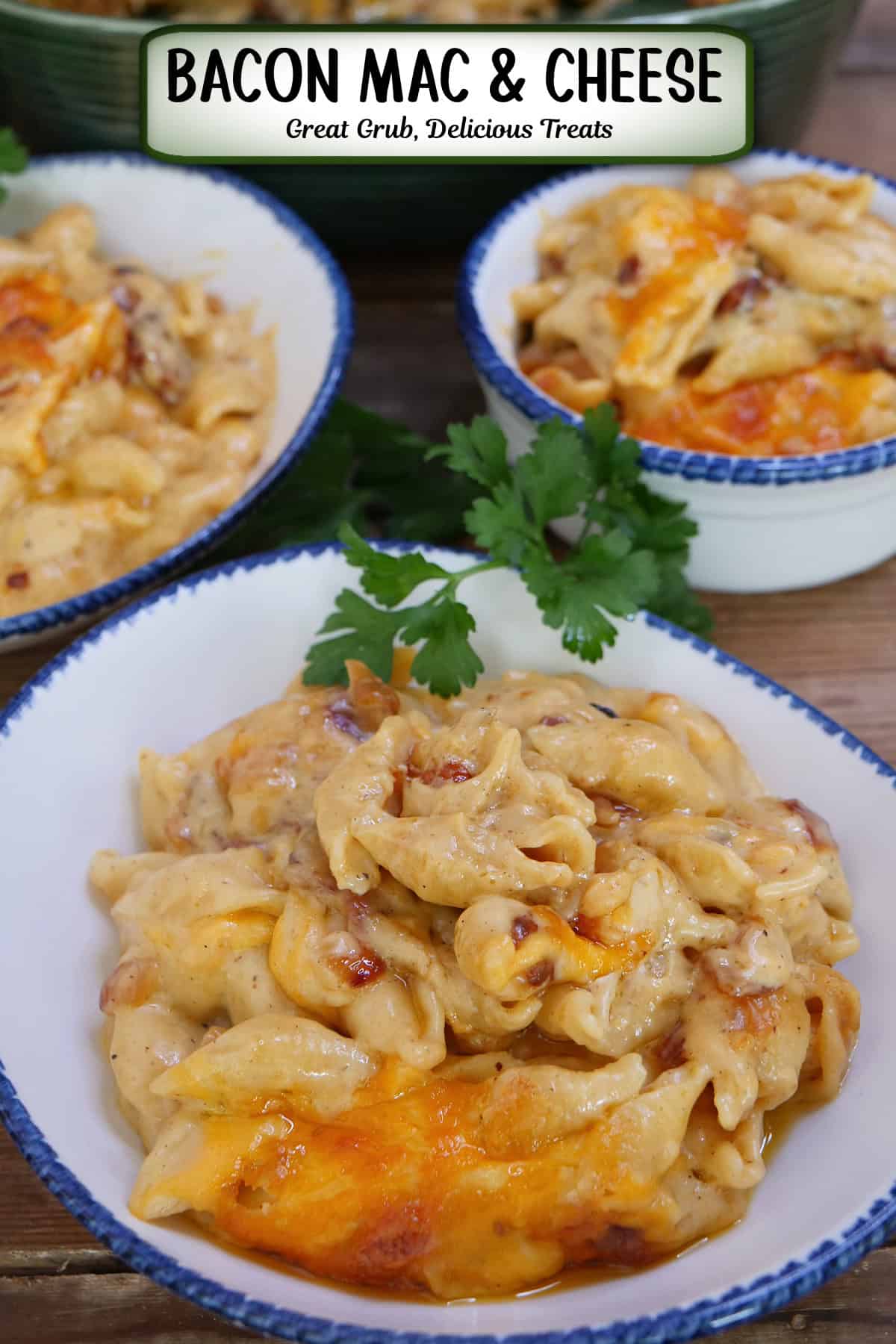 A wood surface with three white bowls with blue trim filled with bacon mac and cheese, and a title overlay at the top.