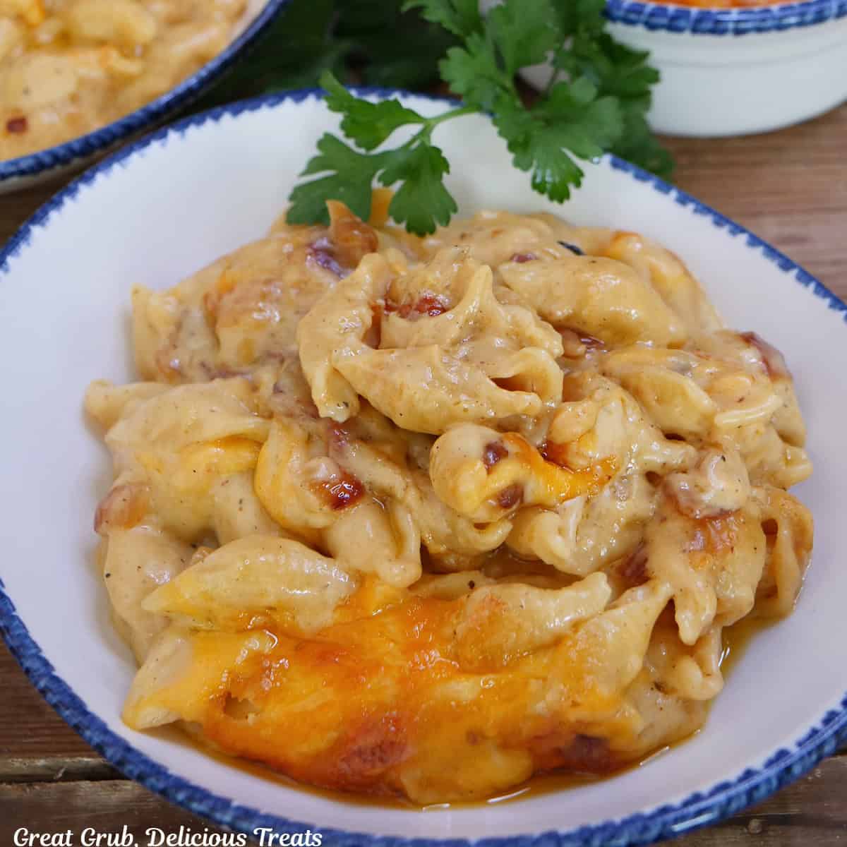 A white bowl with blue trim with bacon mac and cheese in it and the bowl is placed on a wood surface.