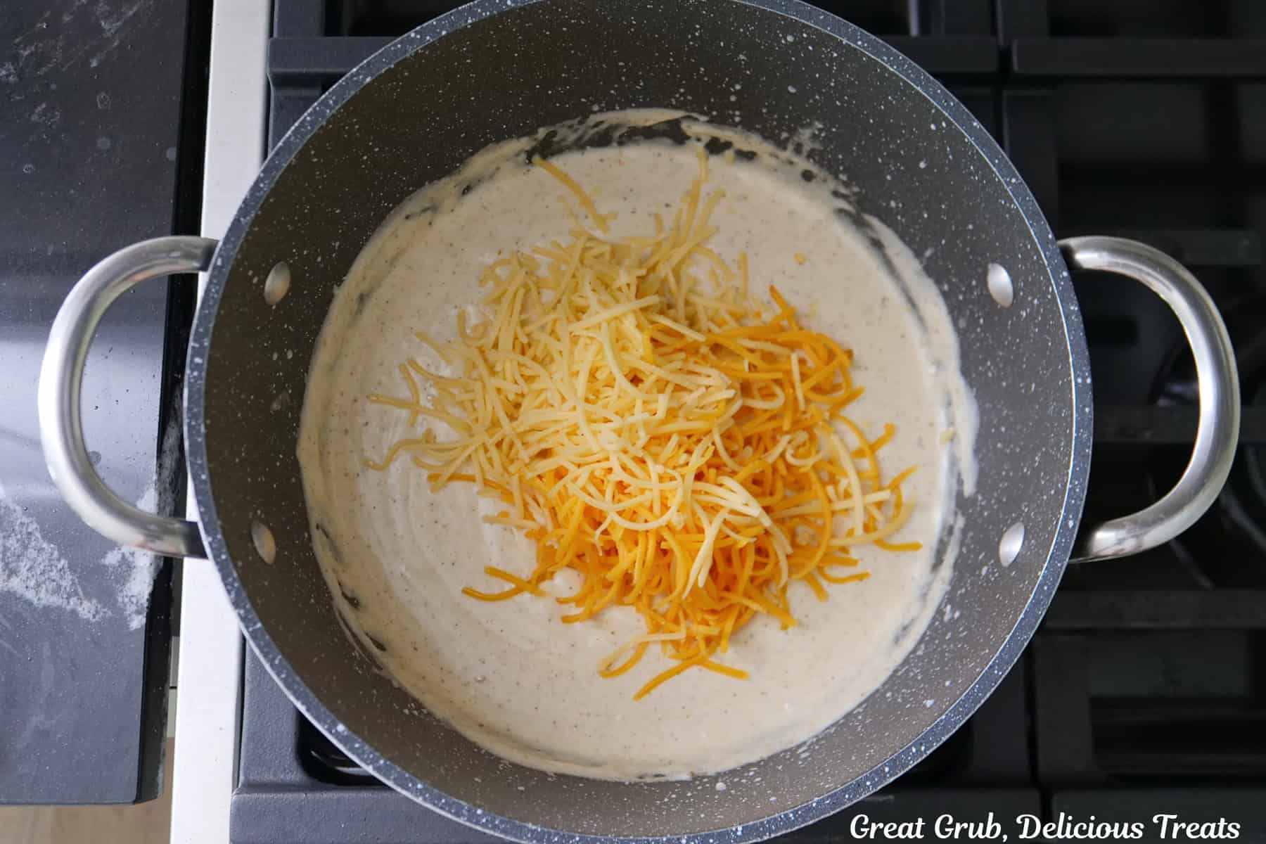 A frying pan with a creamy sauce and two types of shredded cheese added to the pan before being stirred into the sauce.