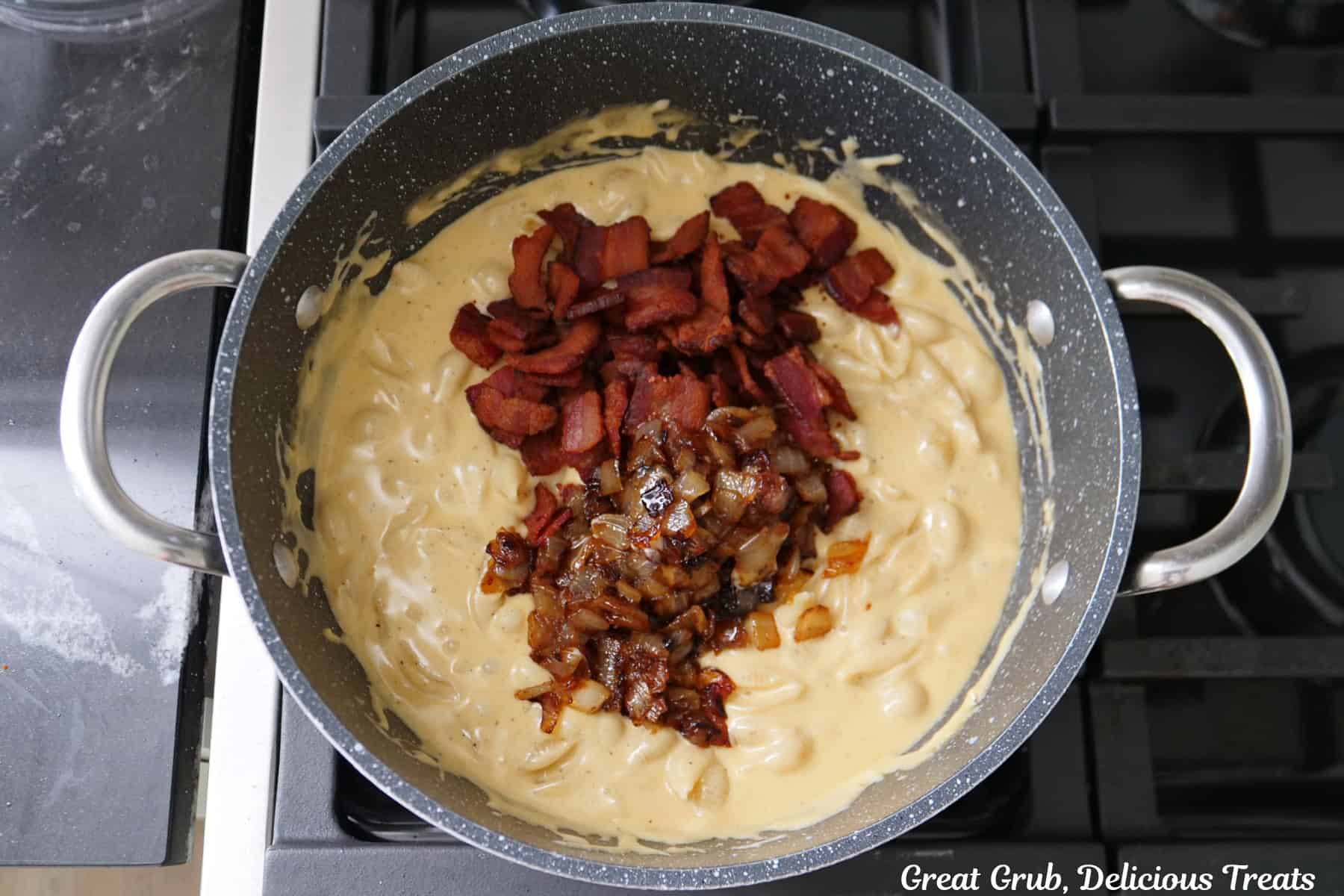 A frying pan with a cheese sauce and the fried bacon pieces and caramelized onions added to the pan.