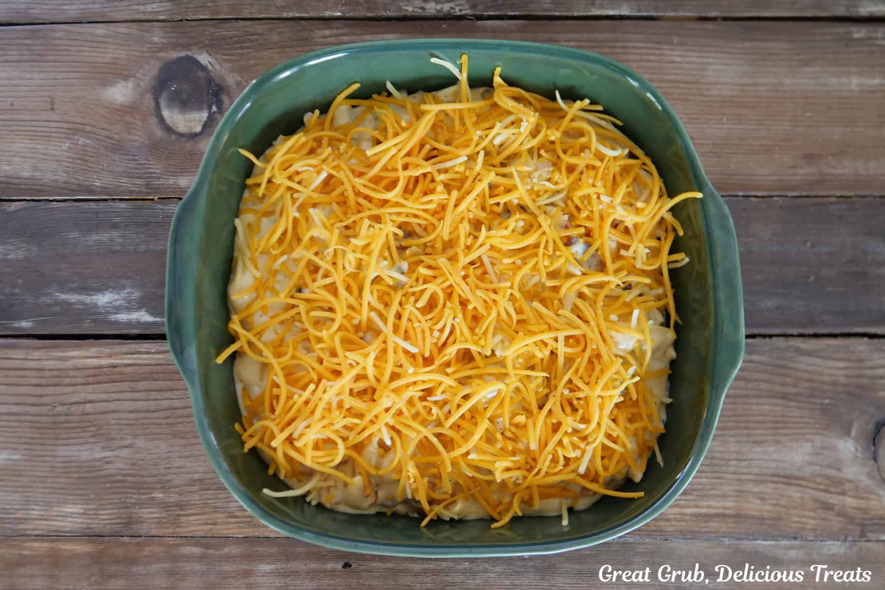 A dark green eight by eight baking dish filled with bacon mac and cheese before going in the oven.
