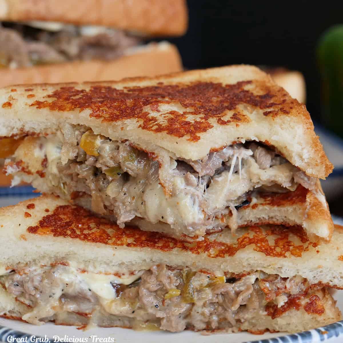 A white plate with blue trim with two halves of a cheesesteak grilled cheese on it with a bite taken out of the top half.