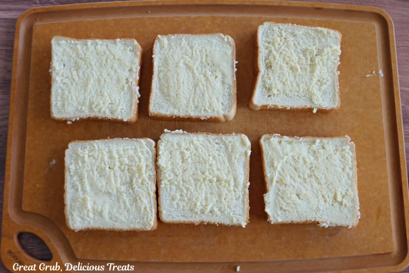 A wood surface with six slices of thick Texas toast bread on it that has been buttered with a cheesy mixture.