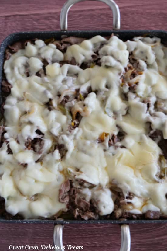 The cheesesteak mixture, in the grill pan, with melted provolone cheese all over the top.