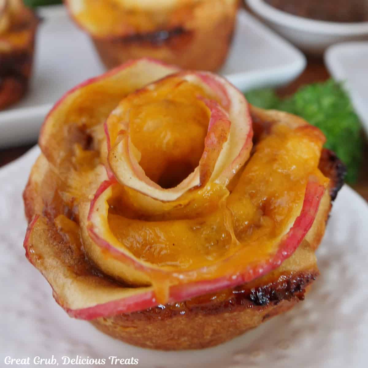 A small round white plate with a cheesy apple pastry rose on it with a title overlay at the top.