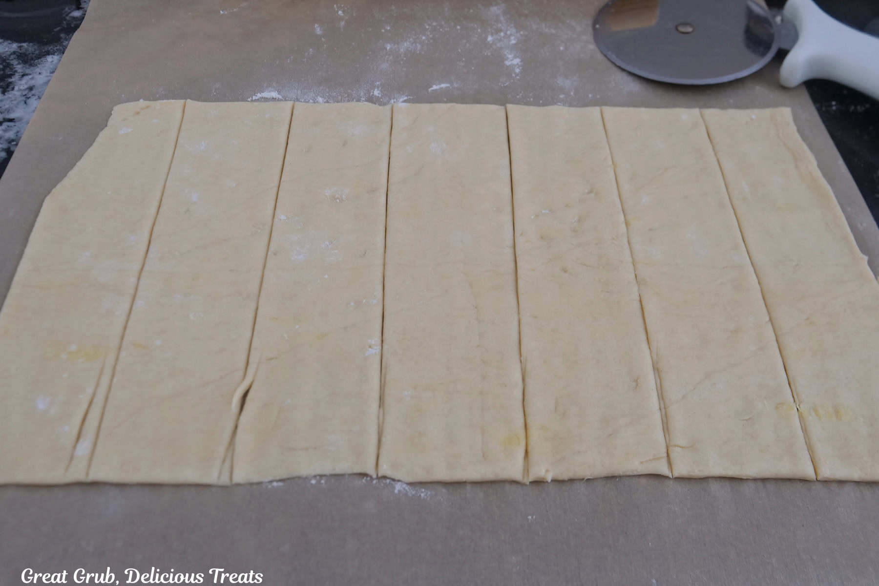 A parchment paper with crescent dough cut into six 2-inch strips.