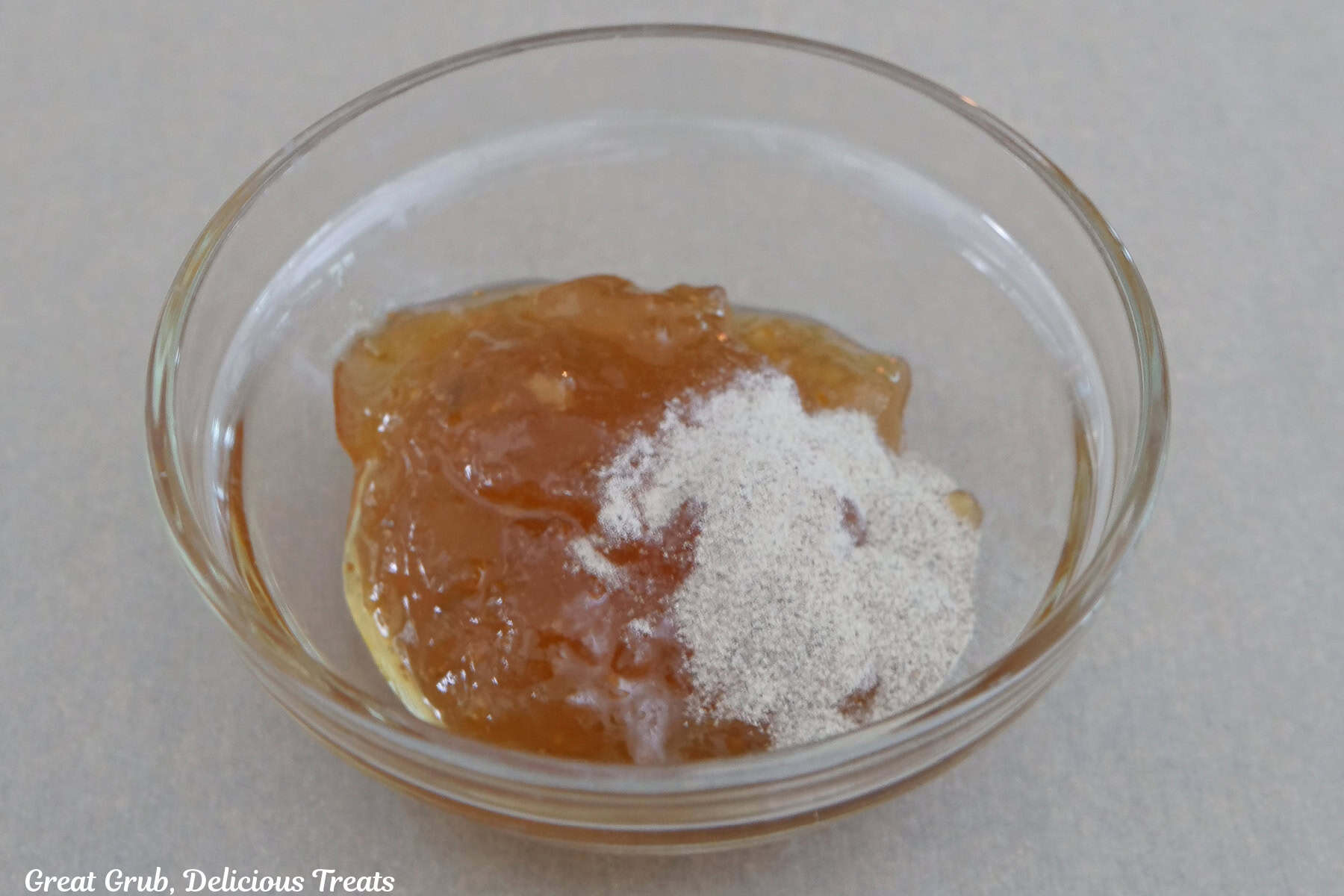 A small glass bowl filled with apricot jam and black pepper before being mixed together.