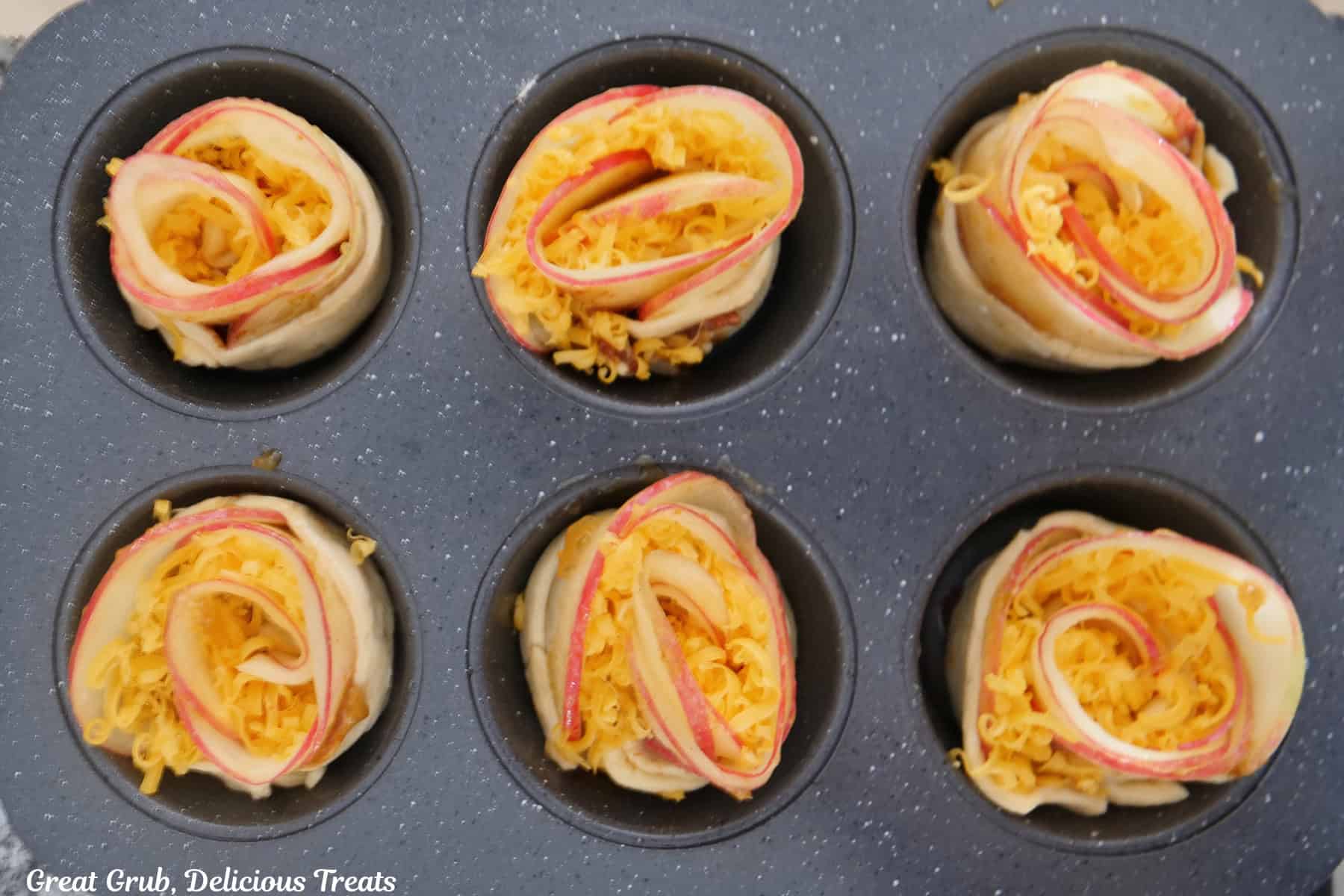 A 6-count muffin tin with cheesy apple pastries in it before being baked.