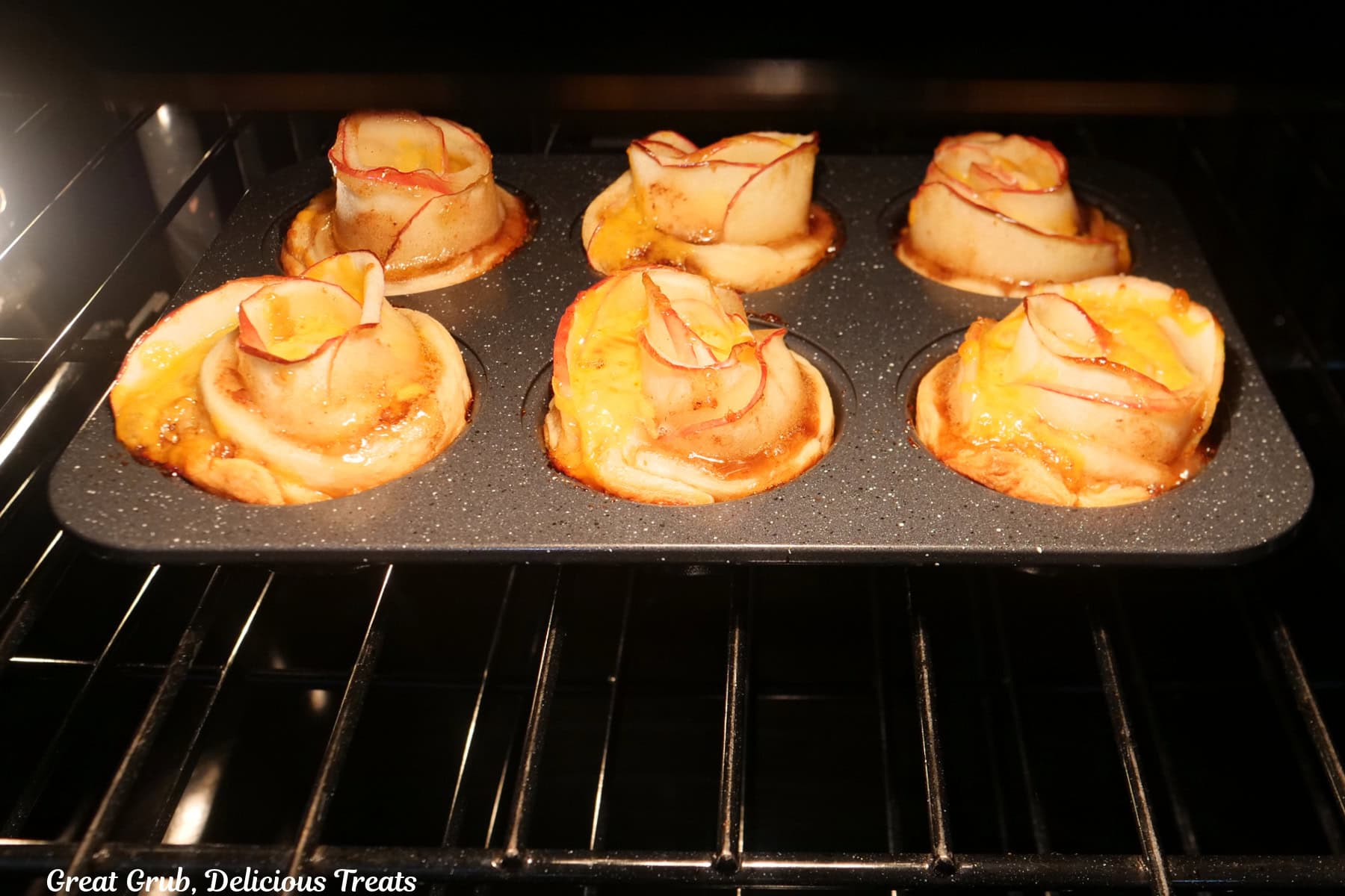 A 6-count muffin tin with six cheesy apple bacon jam roses in it baking in the oven.