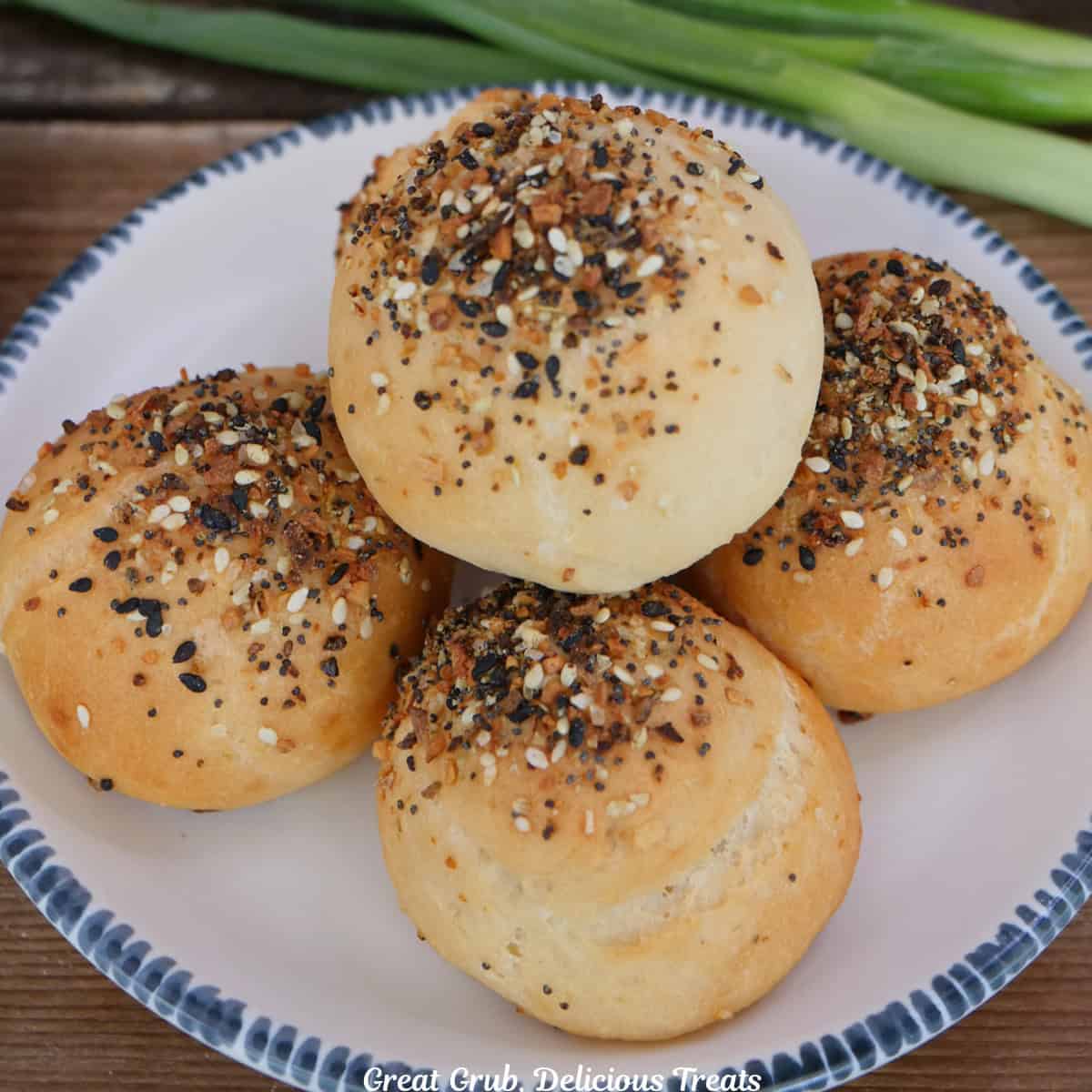 A wood surface with a white round plate with blue trim with five everything bagel bombs on it.