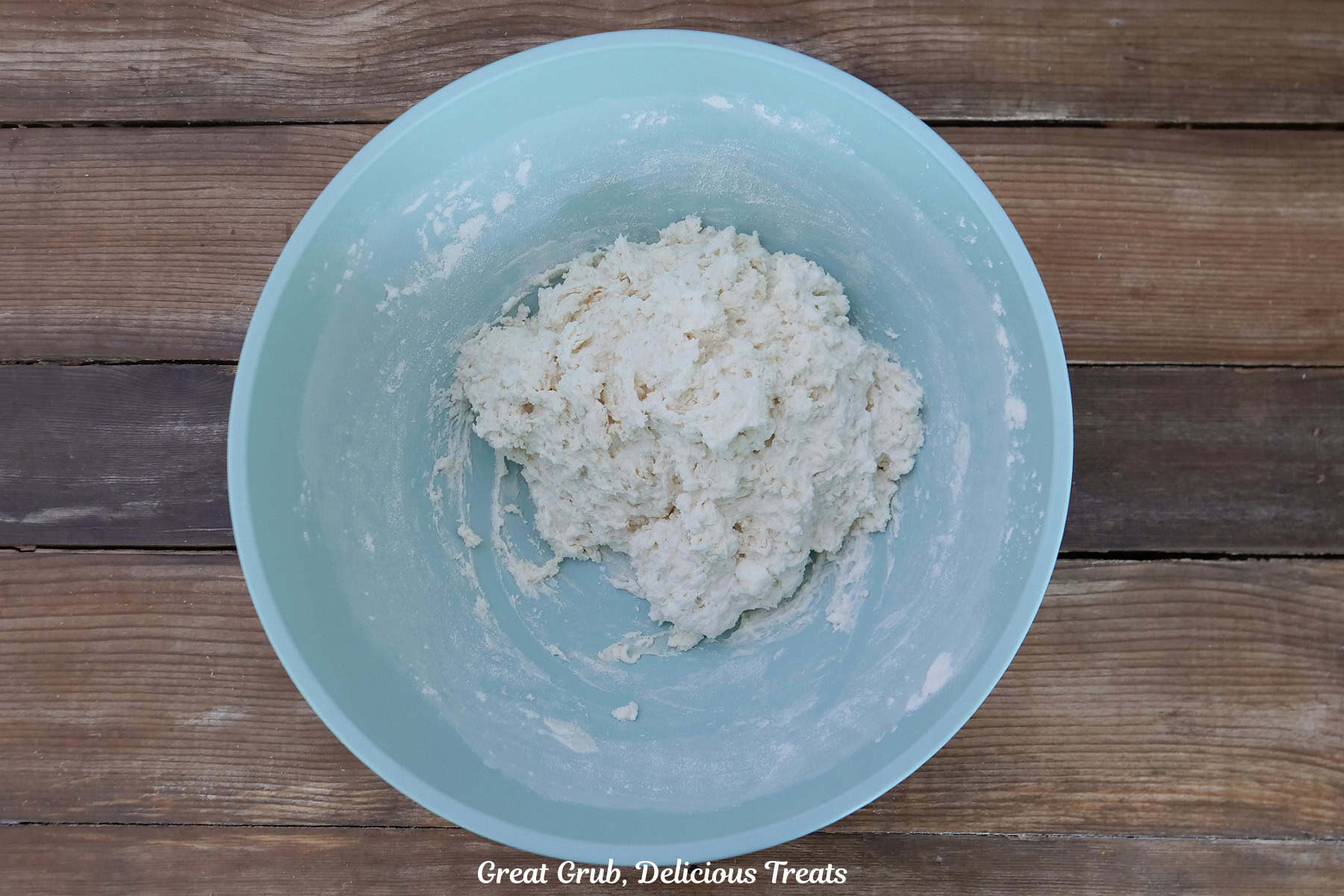 A wood surface with a light blue bowl filled with the bagel bombs dough.
