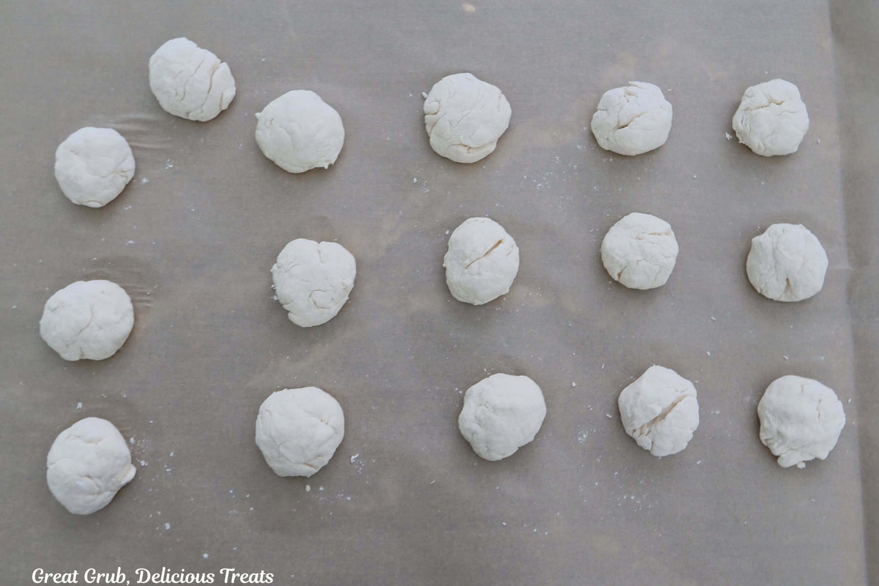 A baking sheet lined with parchment paper with sixteen dough balls on it before being baked.
