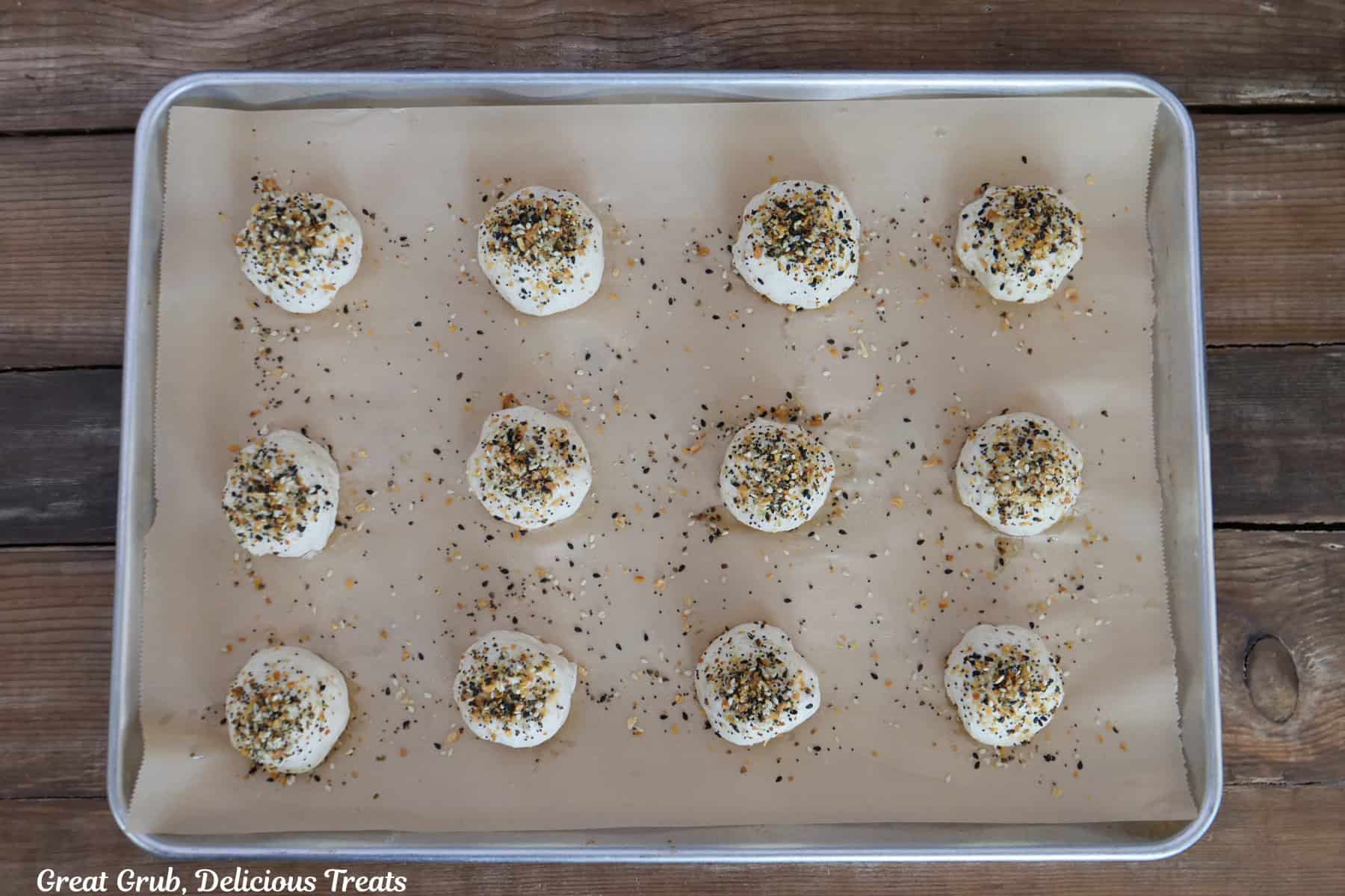 A baking sheet with parchment paper with sixteen bagel bombs topped with Everything Bagel Seasoning sprinkled on them.