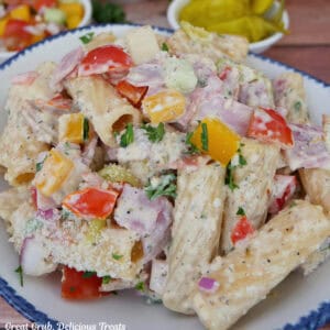 A white bowl with blue trim filled with grinder pasta salad with other ingredients in white bowls placed in the background.