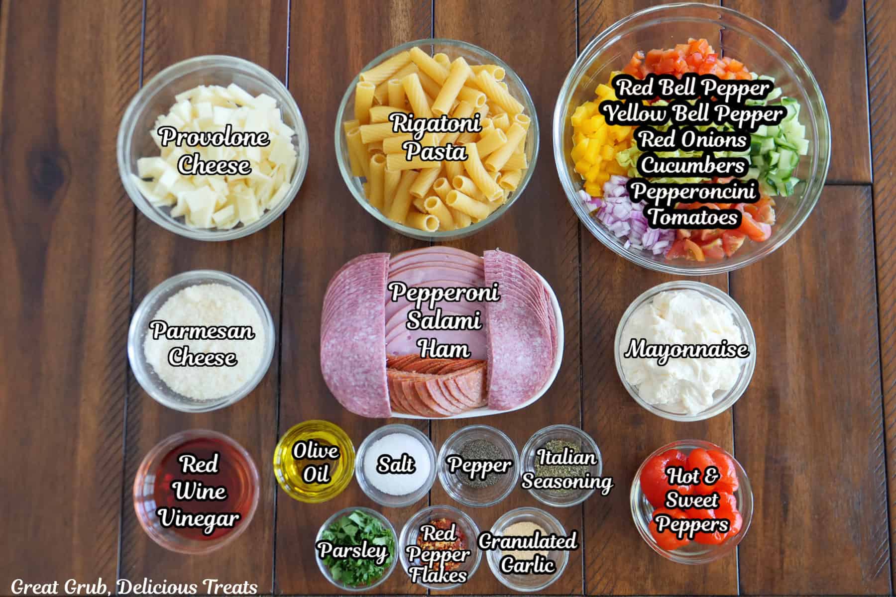 A wood surface with all the ingredients placed on it to make Grinder Pasta Salad.