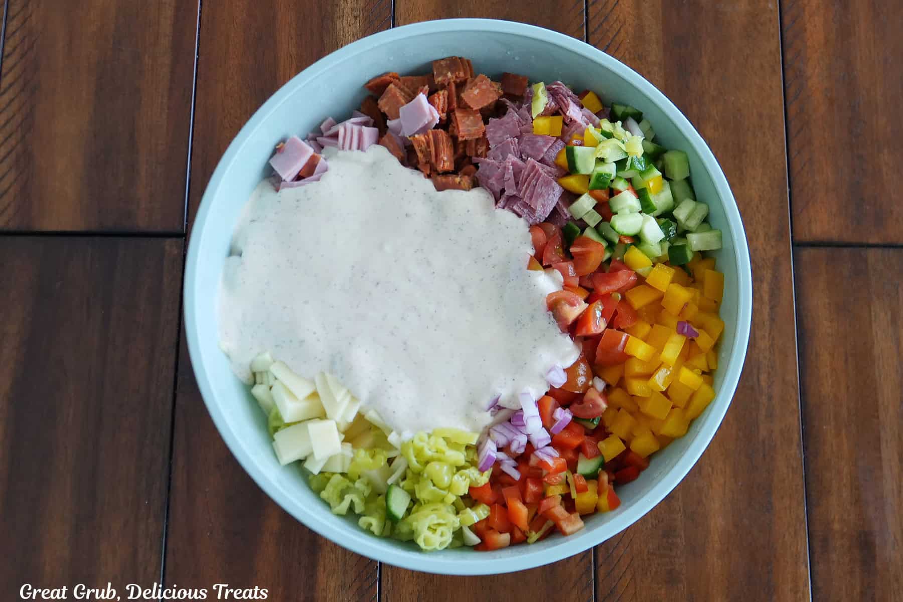 A light blue bowl on a wood surface filled will the chopped ingredients and the creamy sauce added on top before being mixed together.