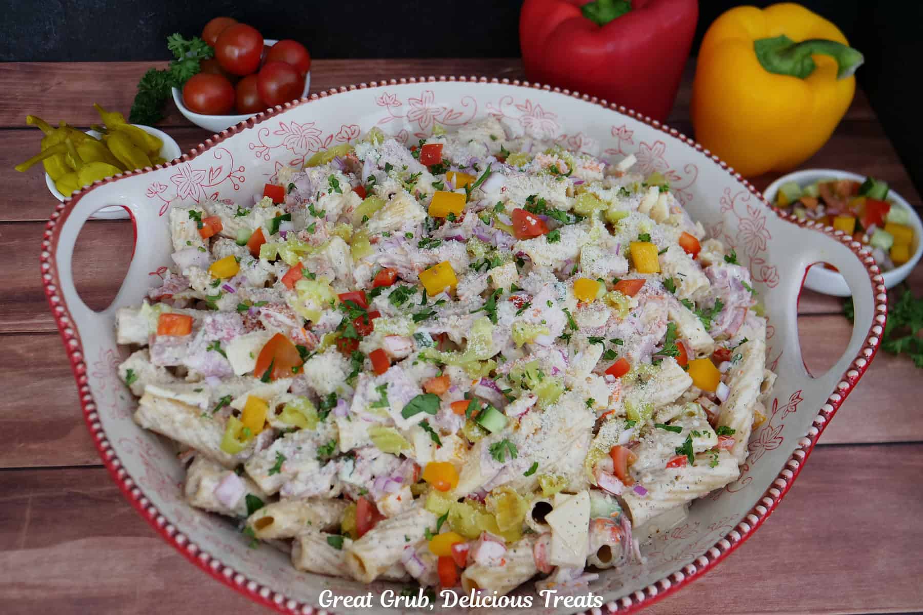A wood surface with a big white and red floral bowl filled with grinder pasta salad.
