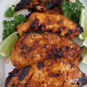 A white plate with four pieces of grilled honey lime chicken on it with lime wedges and parsley placed around them, and a title overlay at the top.
