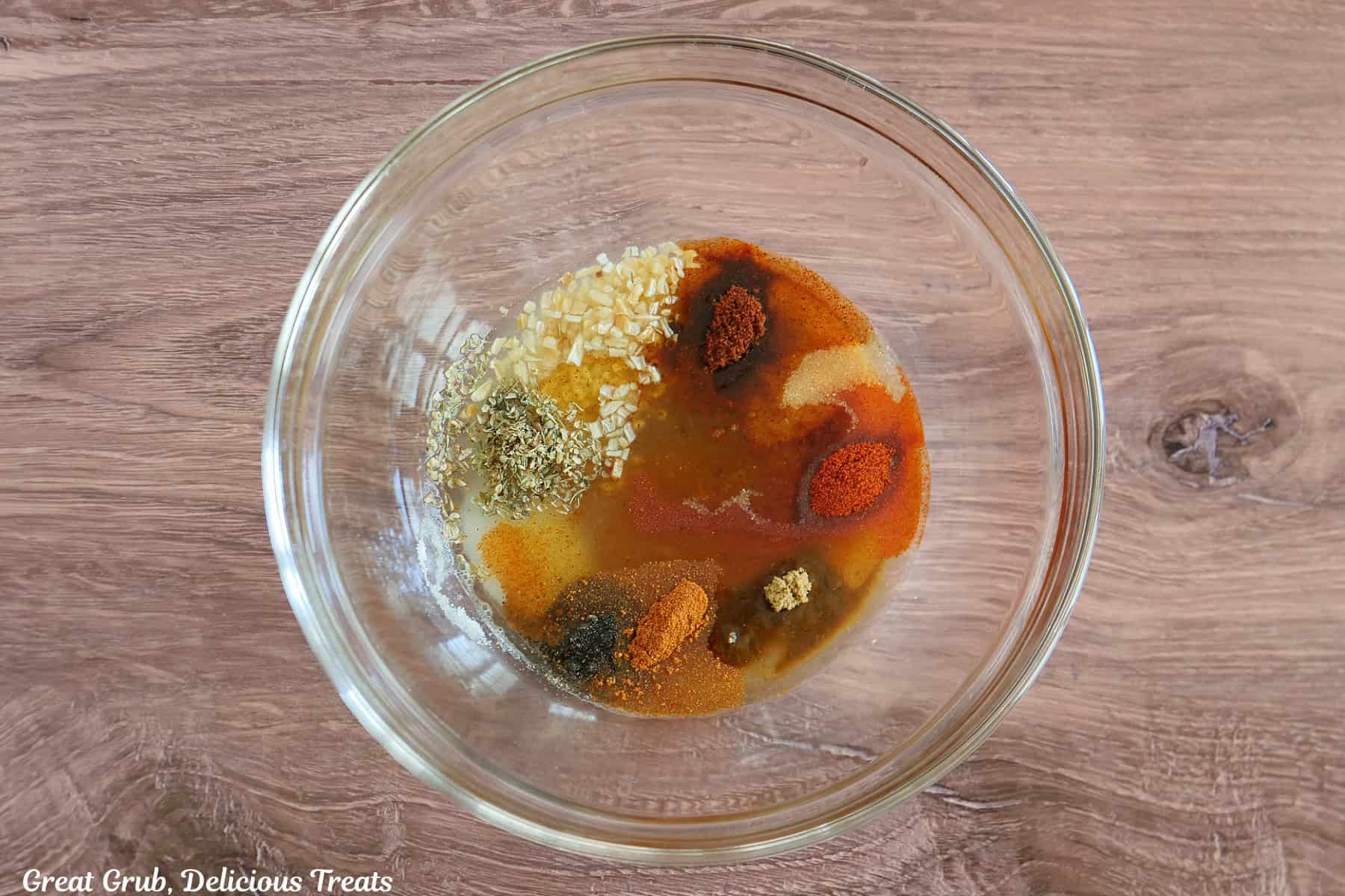 A glass bowl placed on a wood surface with all the ingredients in it to make the honey lime marinade.