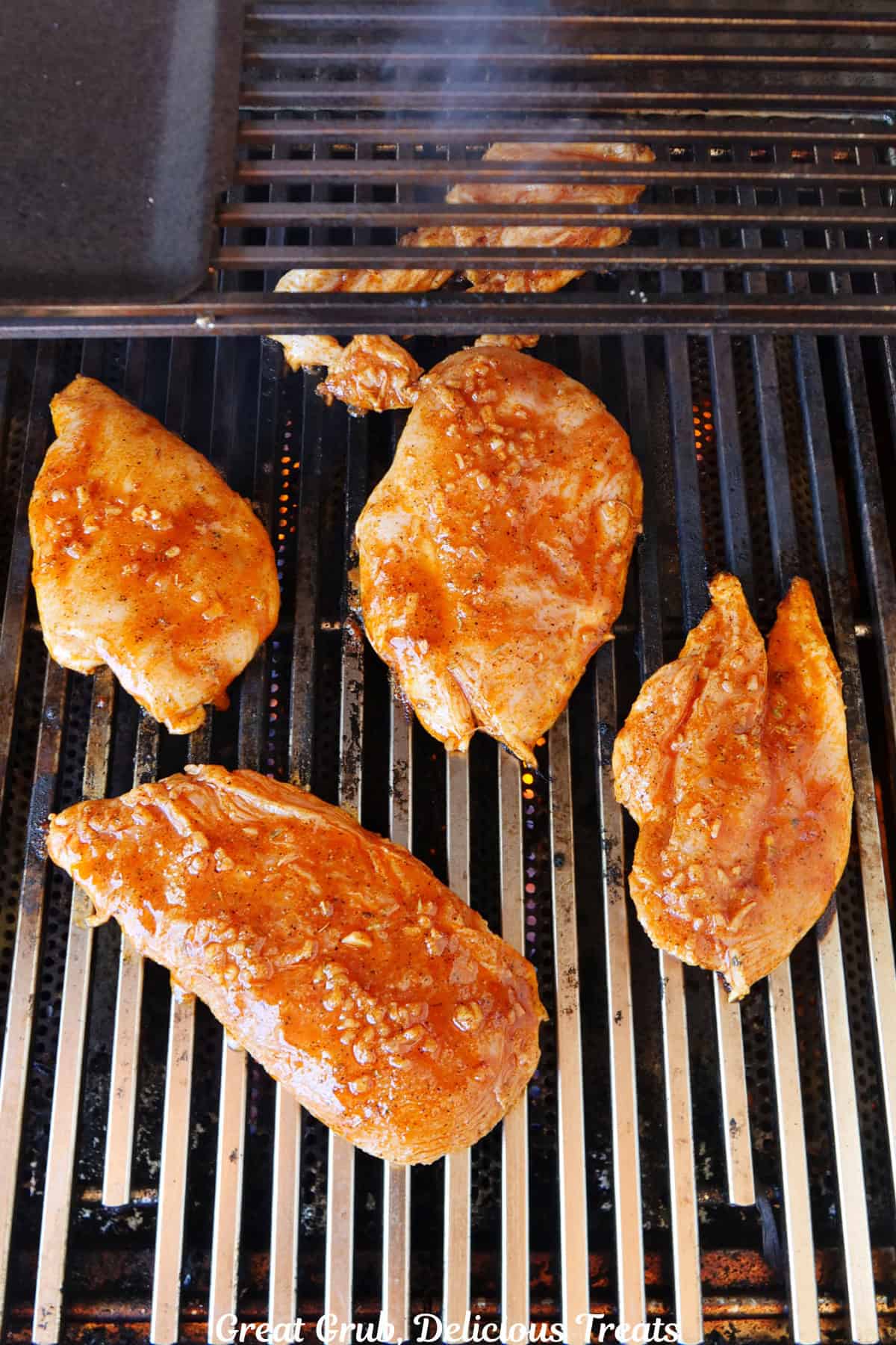 Five chicken breasts grilling on the barbecue.