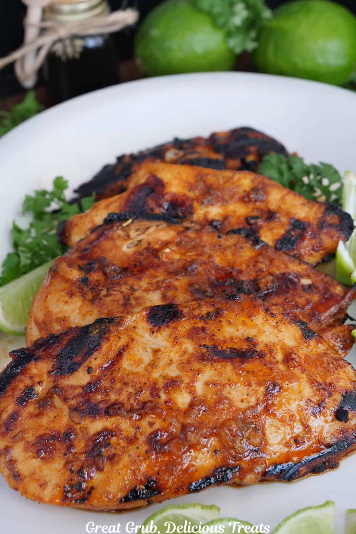 A white oval plate with four grilled honey lime chicken breasts placed on it.