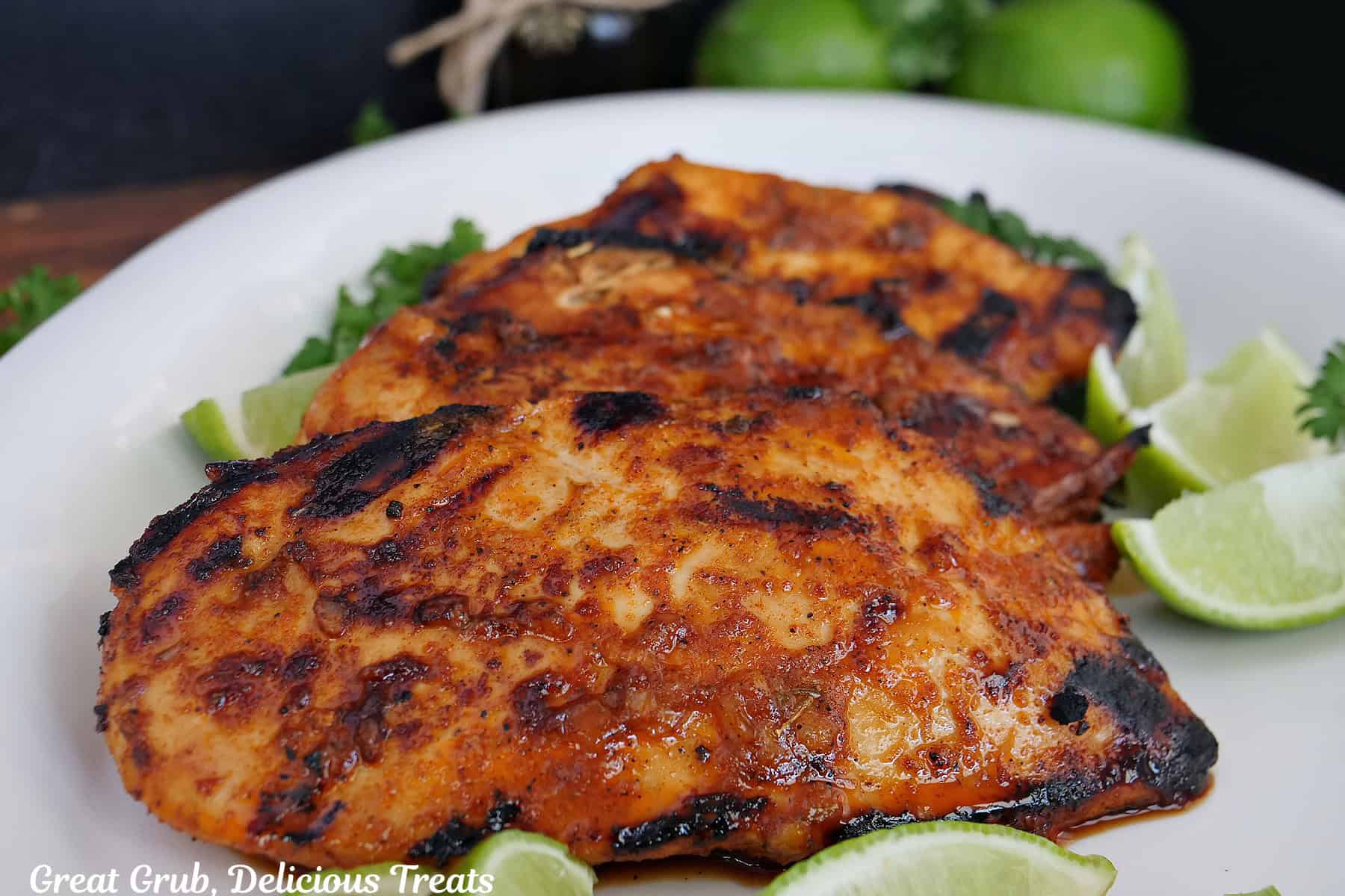 A white oval plate with three grilled honey lime chicken breasts on it.
