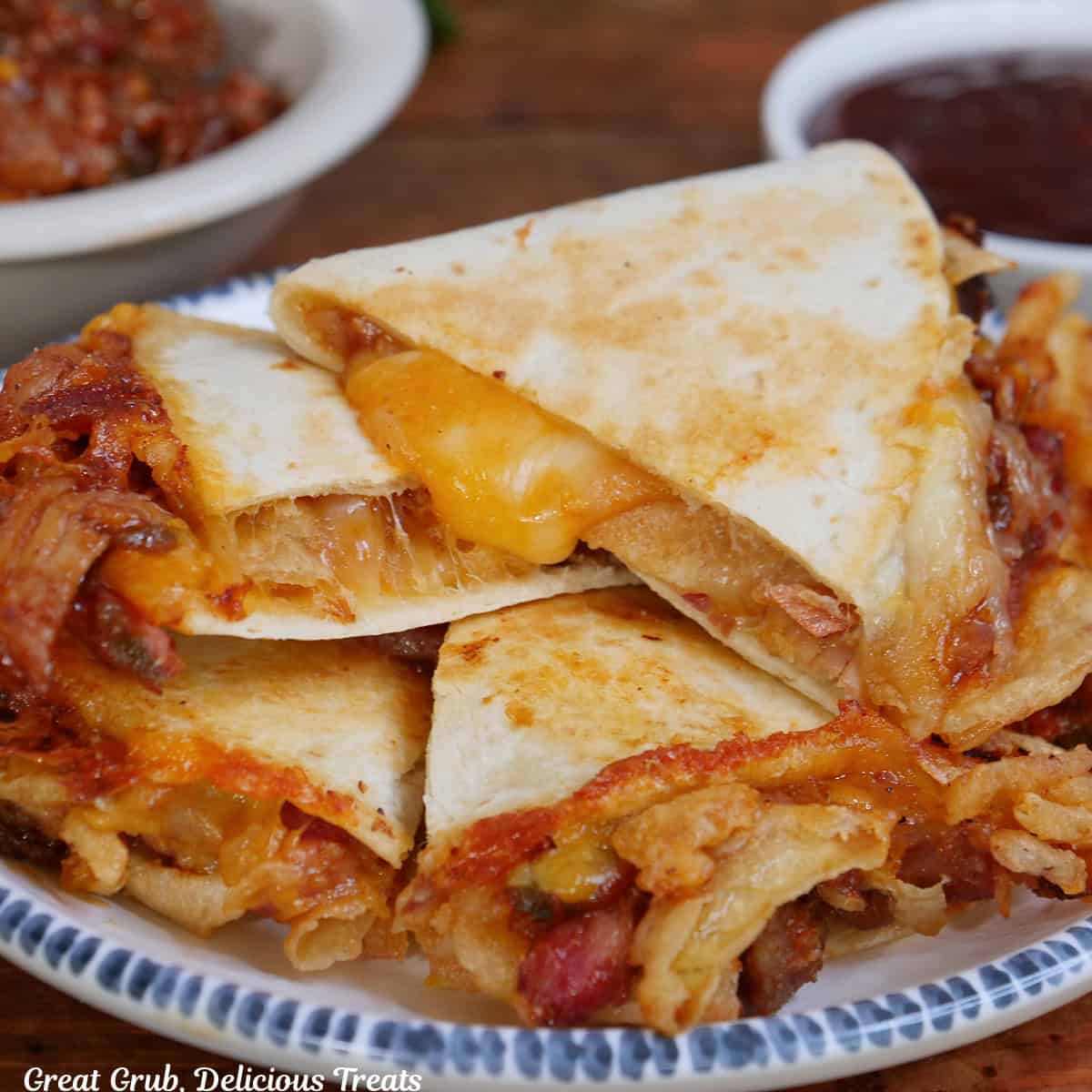 A white plate with blue trim with six wedges of pulled pork quesadillas piled on top of each other.