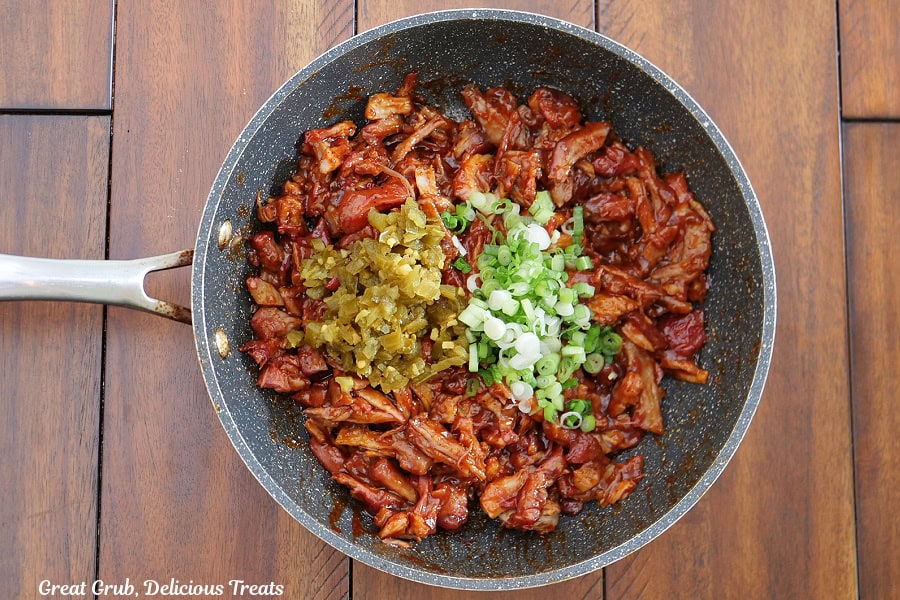 A saucepan filled with barbecue pork with jalapenos and green onions added to it.