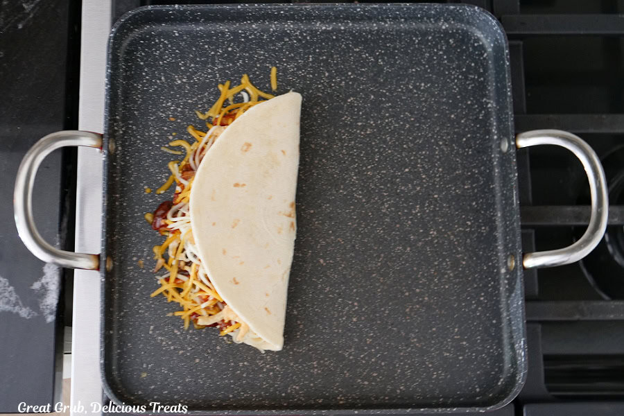 A square frying pan with a pulled pork quesadilla in it with the tortilla folded in half.