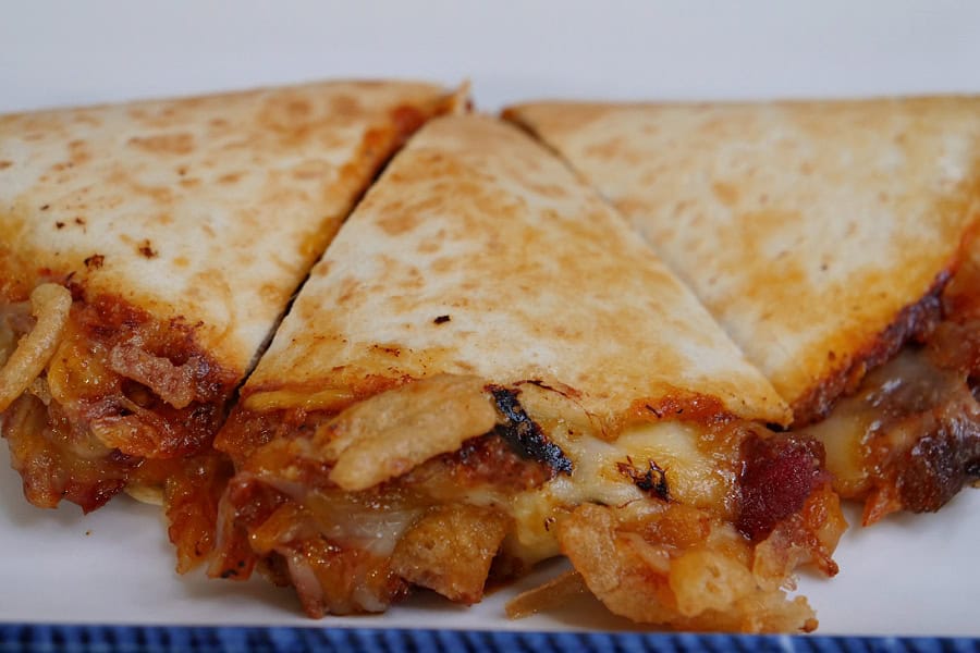 A white oblong plate with blue trim with a quesadilla on it that has been cut into three wedges.