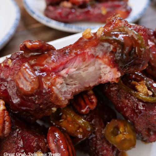 A round white plate with blue trim with three smoked ribs on a bed of vegetable rice with a bite taken out of the top rib.