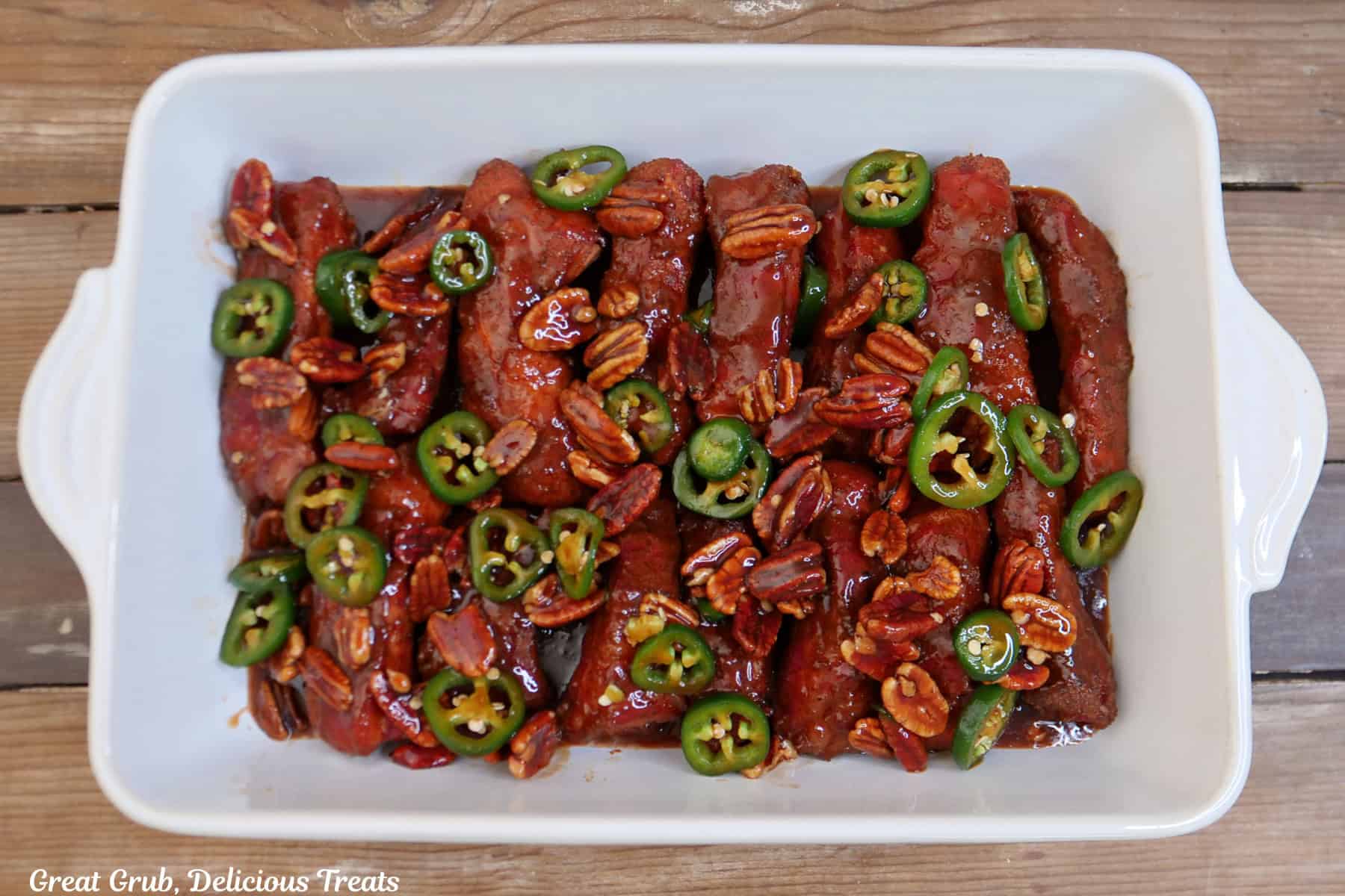 A 13 by 9 white baking dish with the partially smoked ribs in it with the maple pecan jalapeno barbecue sauce poured over the top.