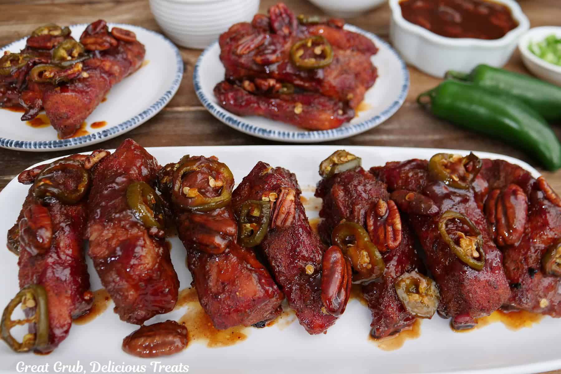 A oblong white plate with two other round white plates with smoked pork ribs on them.