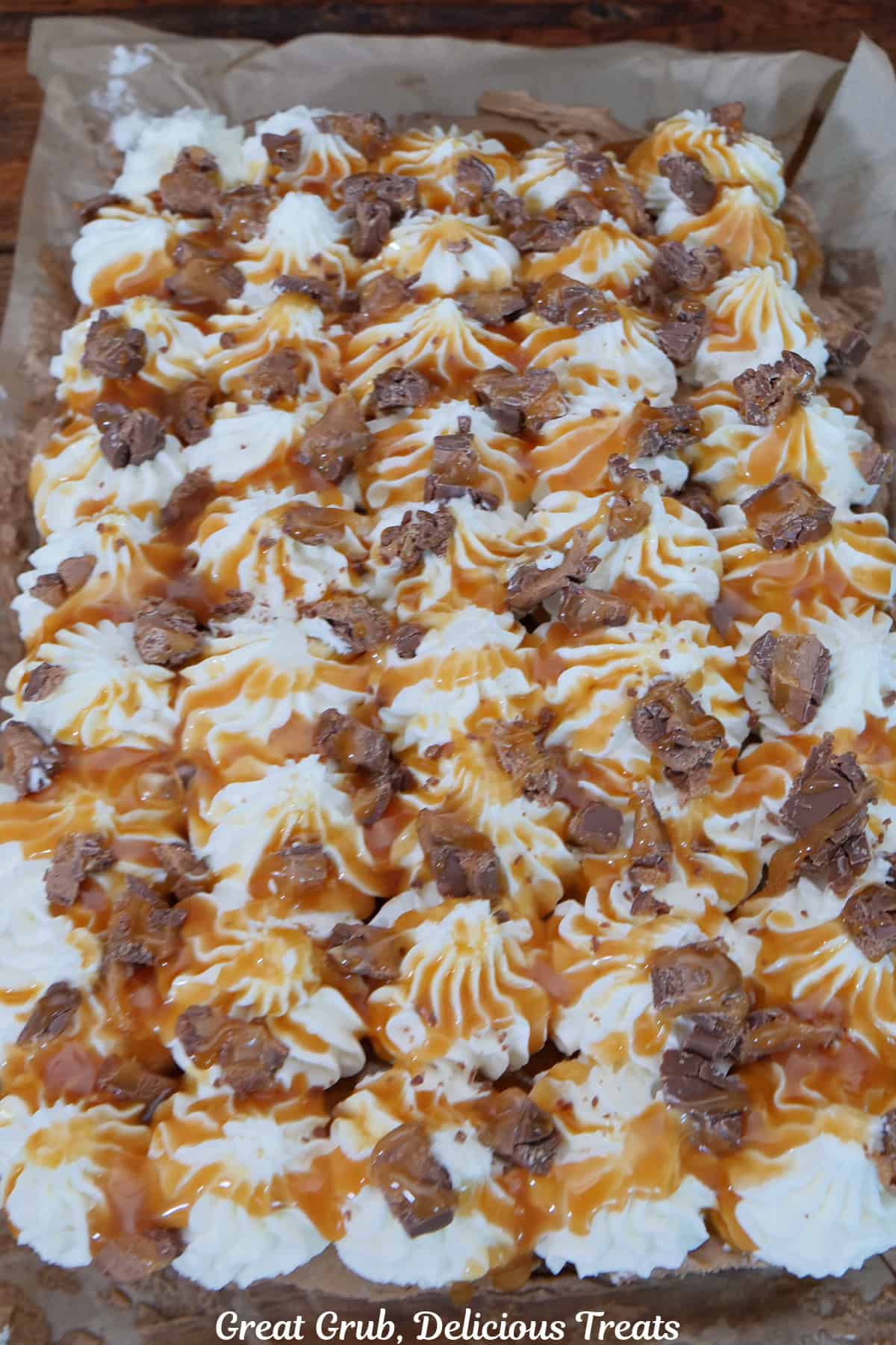 A 7 by 11 glass baking dish with a Milky Way dessert in it that is topped with whipped cream, caramel sauce, and coarsely chopped milky way candy bar on top.
