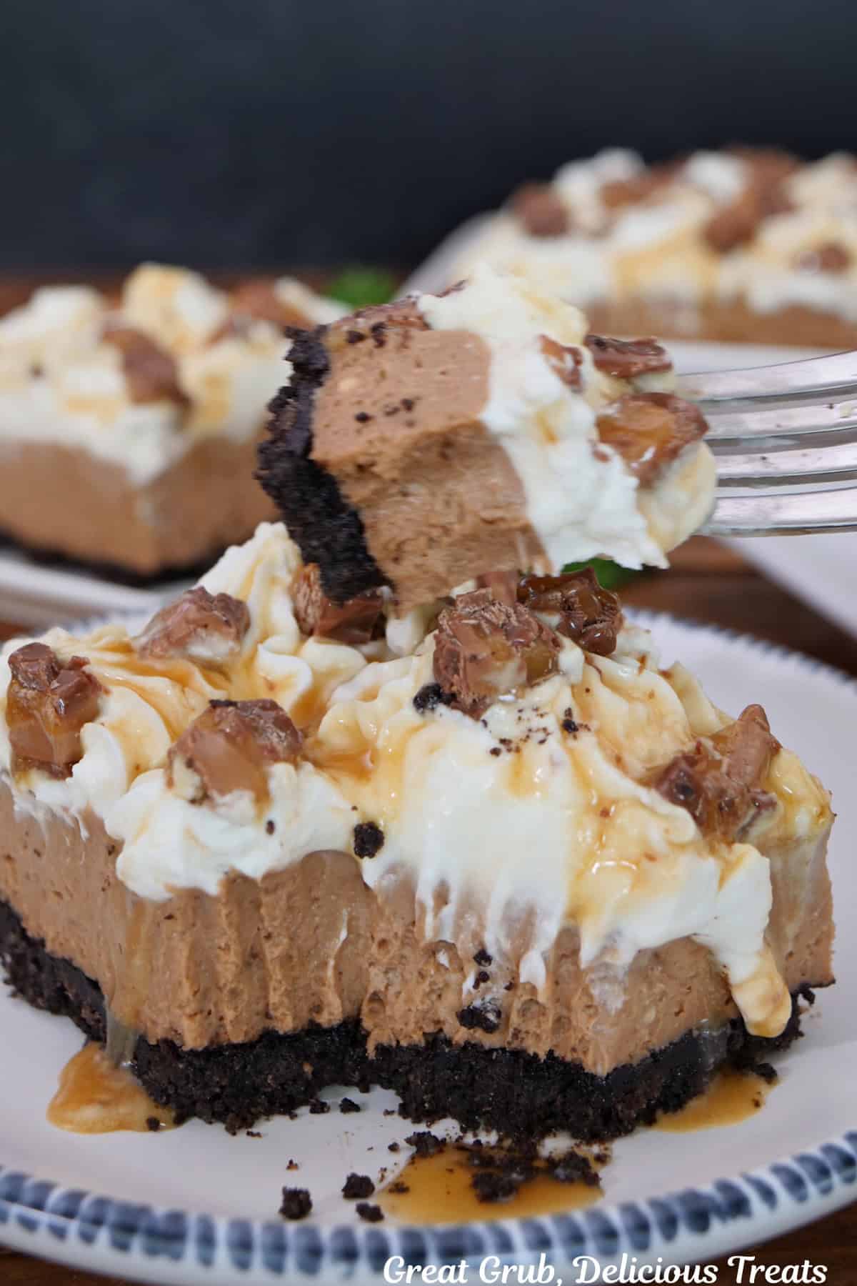A bite of milky way cream cheese dessert on a fork held over the plate with a slice of dessert on it.