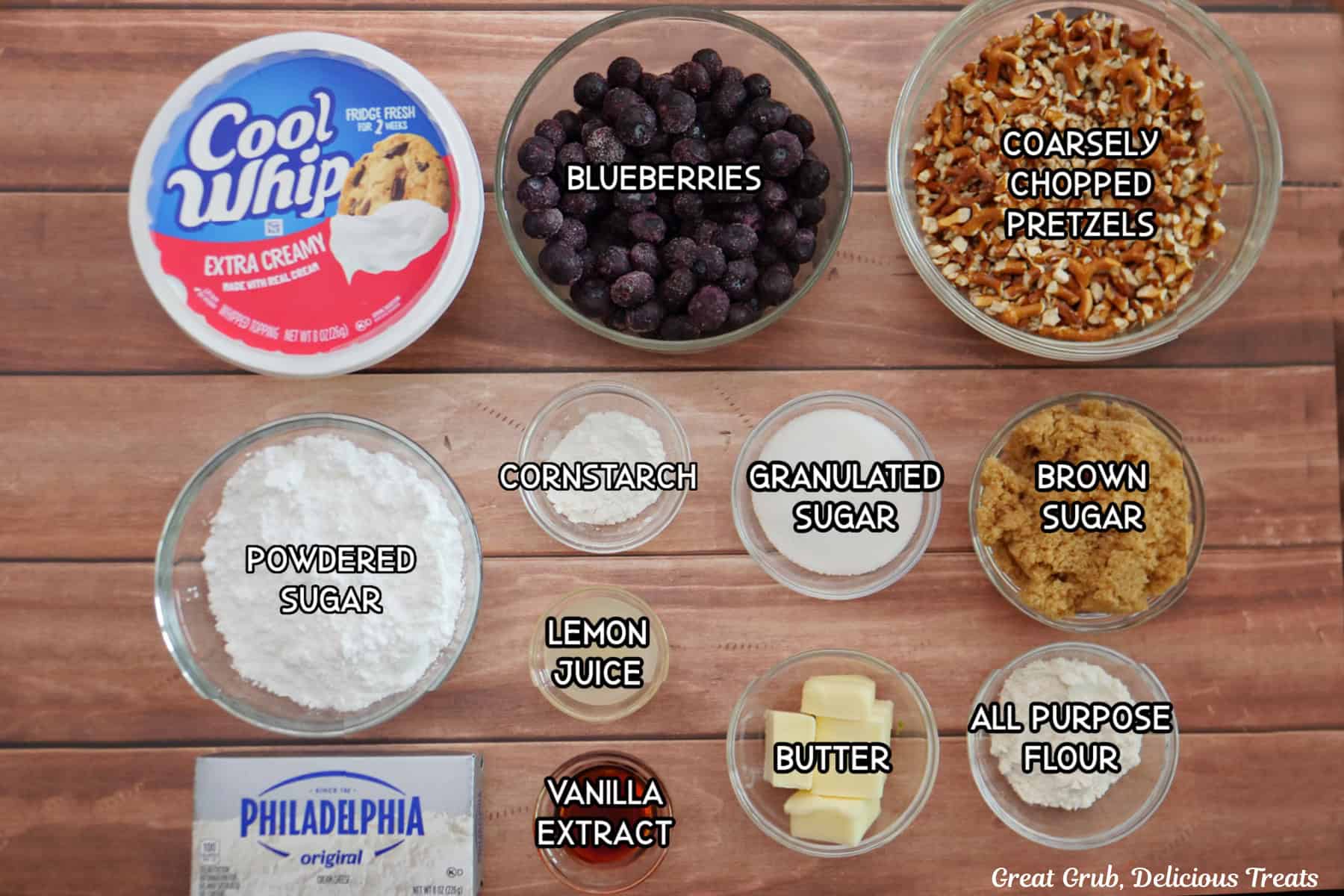 A wood surface with all the ingredients placed on it to make mini blueberry pretzel desserts.