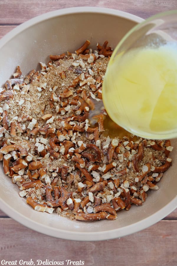 A white mixing bowl with the pretzel ingredients in it and melted butter being added to the mixture.